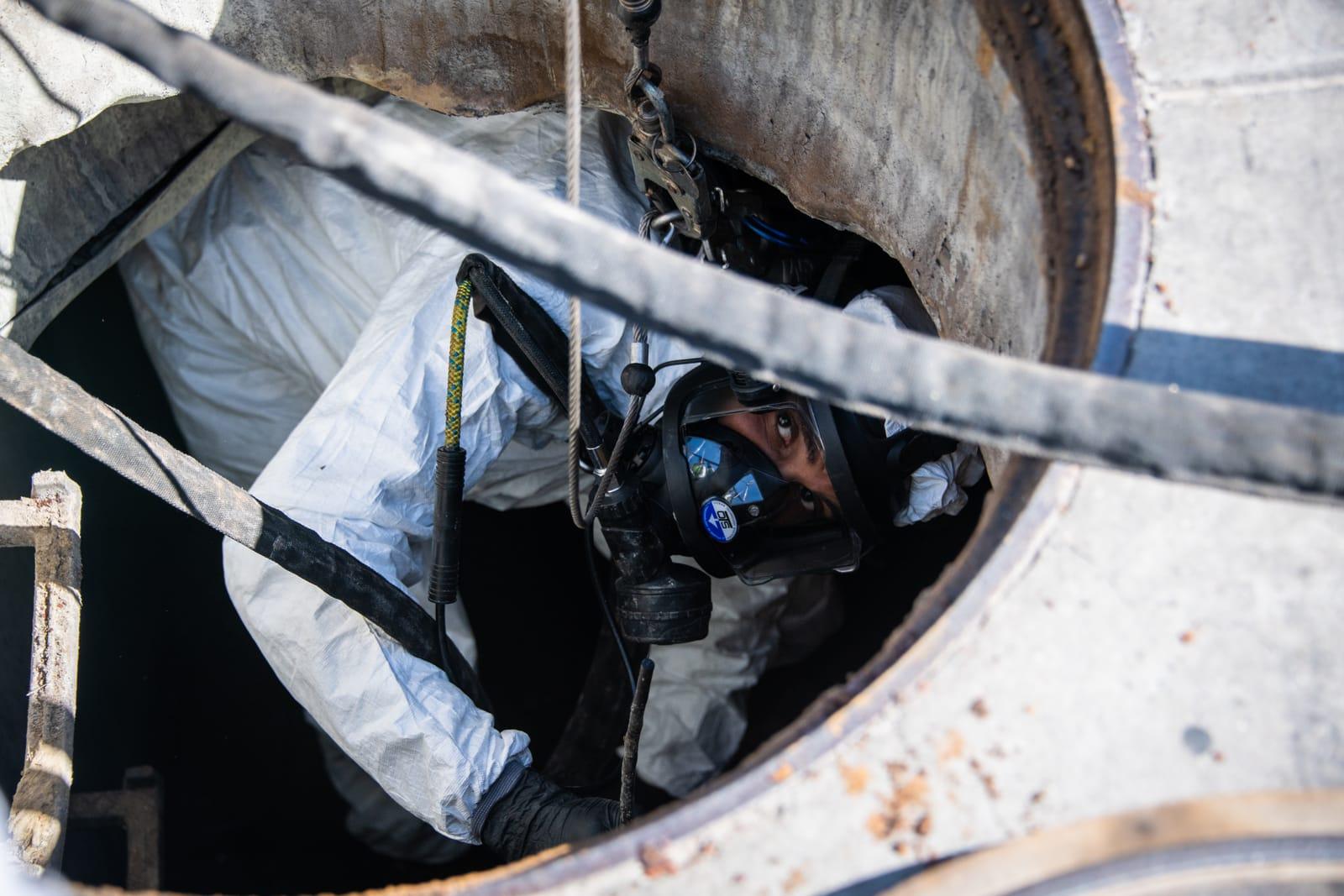 Masked technician looking up from inside a manhole