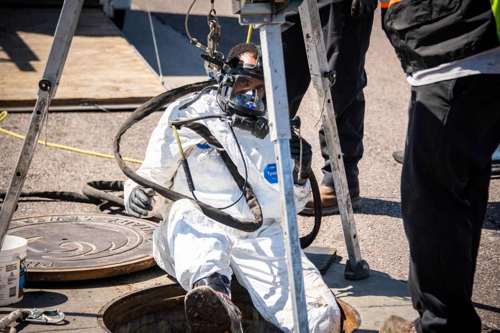 Fully suited technician entering a manhole on air lines