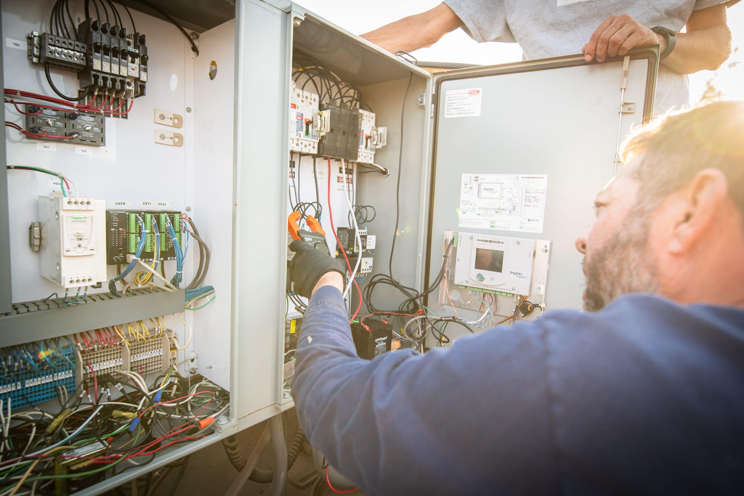 Technician wiring inside an open control panel at sunset